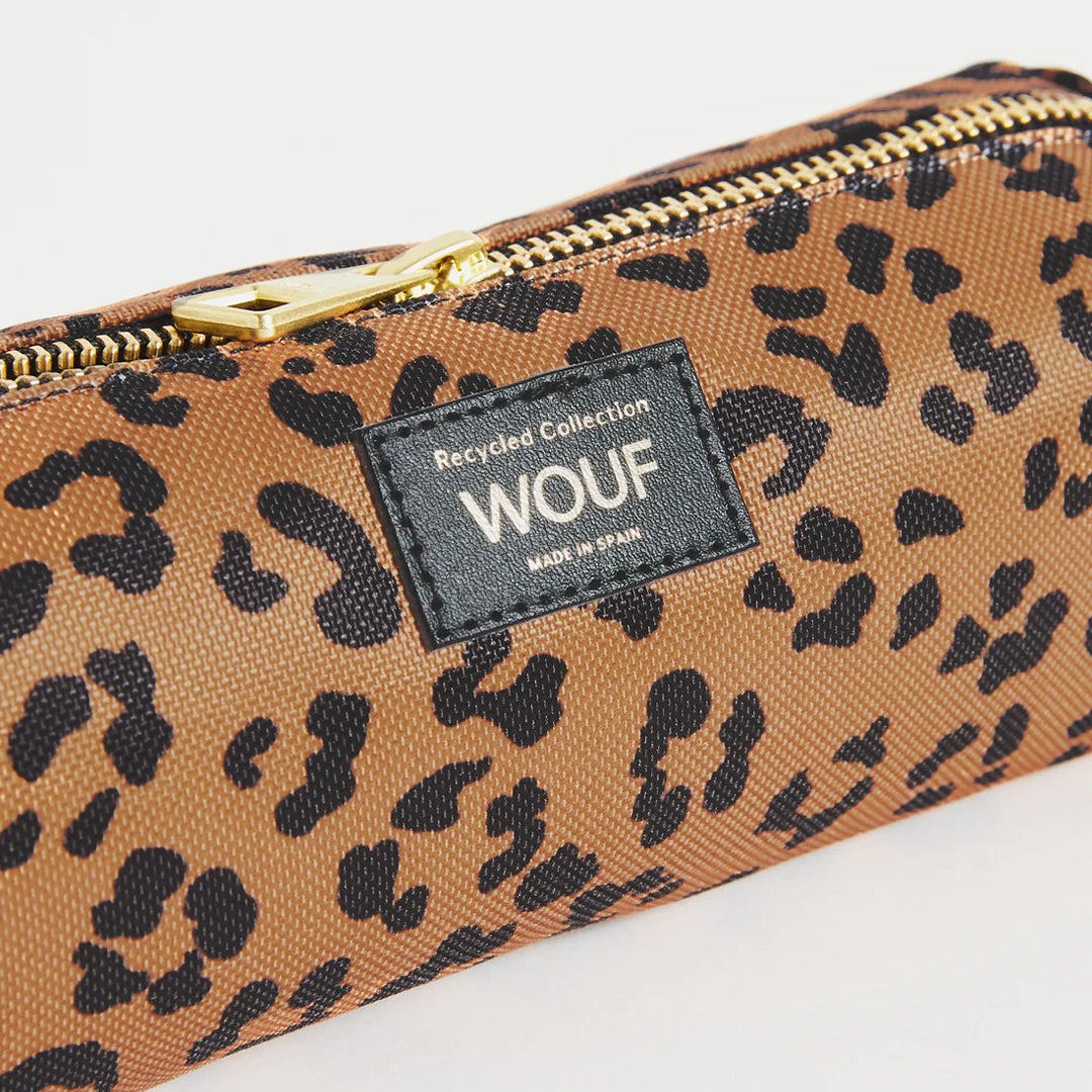 Vue rapprochée de la trousse WOUF montrant l'étiquette avec le logo et le texte "Recycled Collection" sur un fond d'imprimé léopard avec fermeture éclair dorée