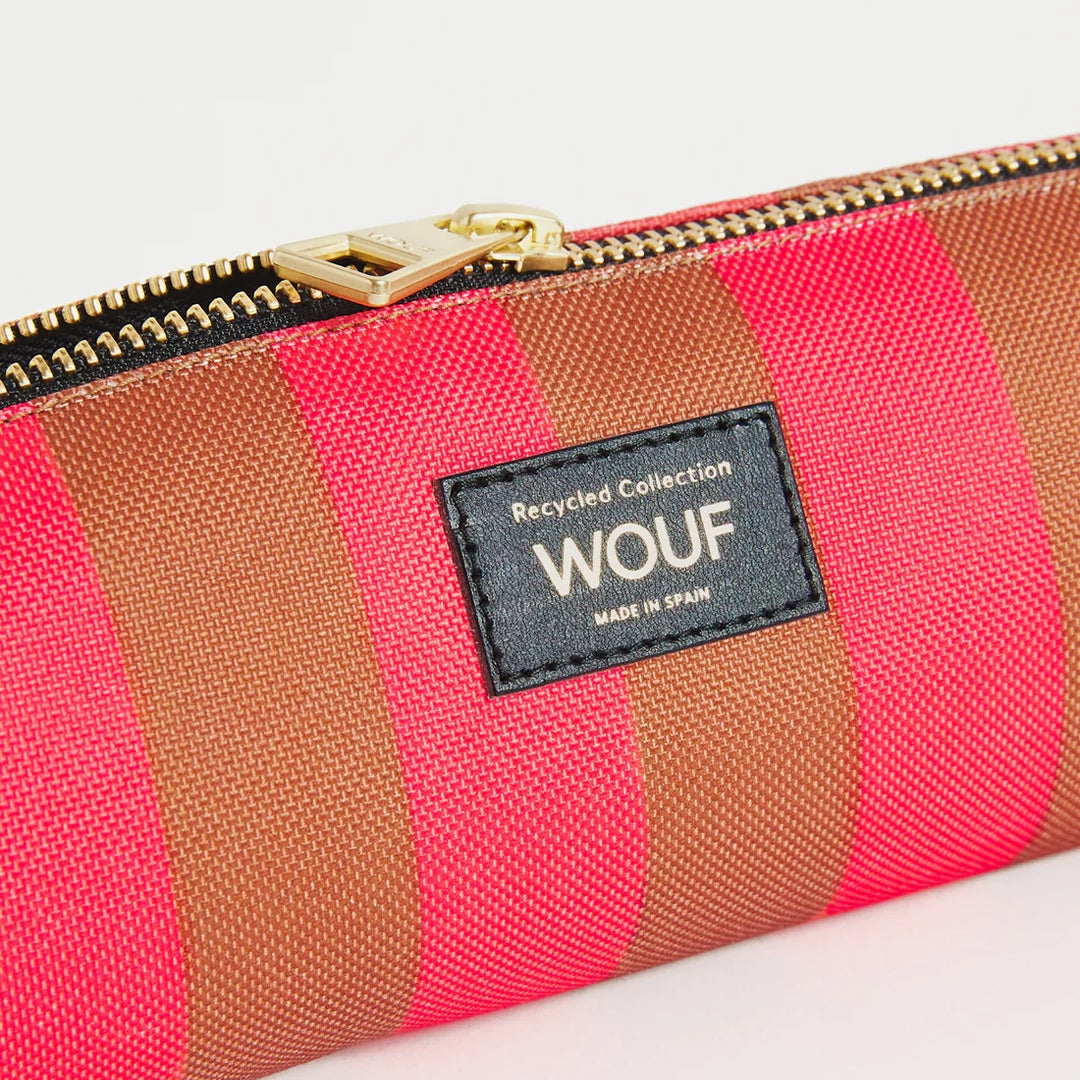 Vue rapprochée de la trousse WOUF montrant l'étiquette avec le logo et le texte "Recycled Collection" sur un fond de rayures rouges et brunes avec fermeture éclair dorée, inspirée par des motifs vintage