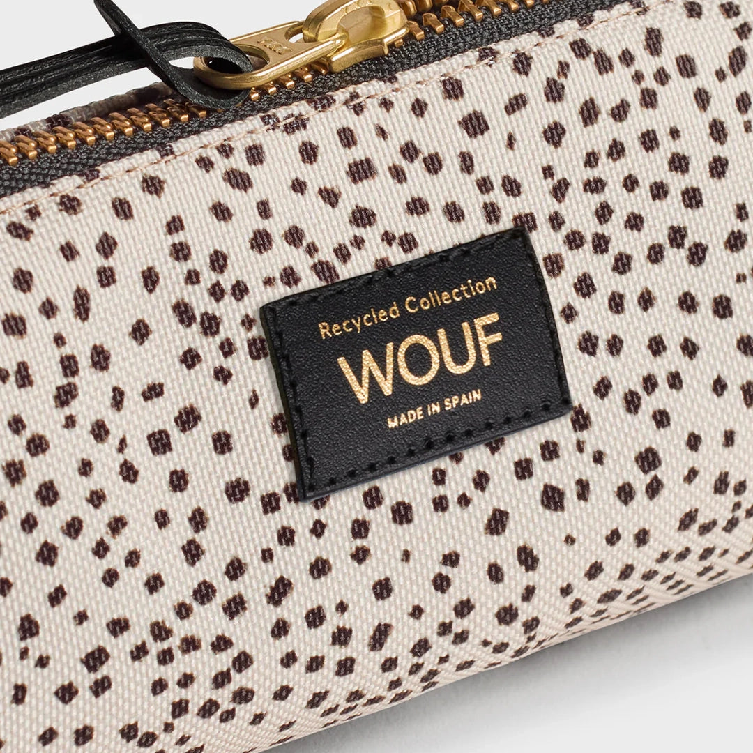 Vue rapprochée de la trousse WOUF montrant l'étiquette avec le logo et le texte "Recycled Collection" sur un fond d'imprimé à pois marron avec fermeture éclair dorée