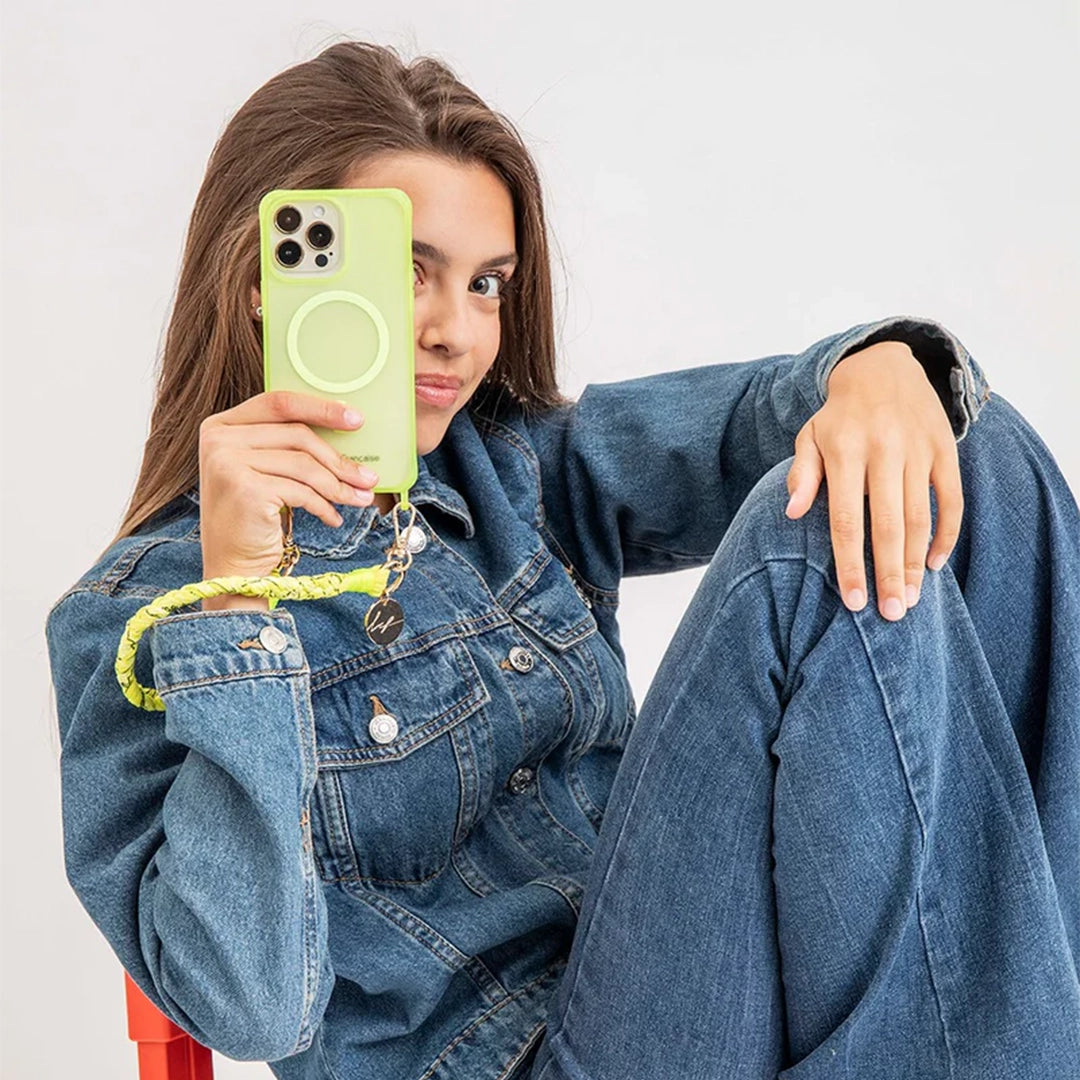 Mode de vie avec le Collier Bandana Tressé - Della - Jaune Fluo : Une jeune femme portant une tenue en jean, utilisant le collier Della jaune fluo comme bracelet, fixé à son téléphone avec une coque verte, illustrant la polyvalence et le style du collier.