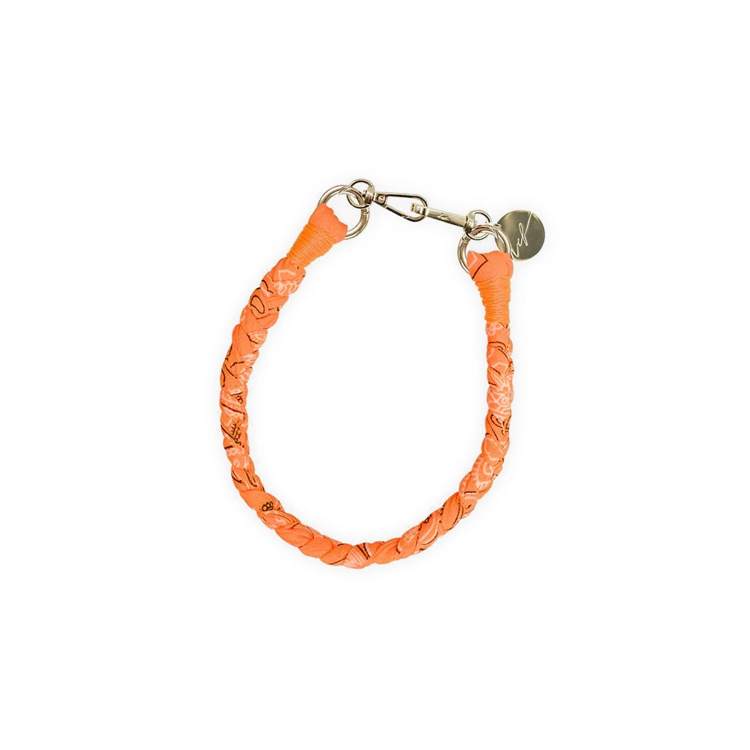 Un collier tressé en tissu bandana orange fluo, équipé de mousquetons dorés et d'une médaille gravée "LCF". Le design unique et vibrant ajoute une touche de style audacieuse à toute tenue.