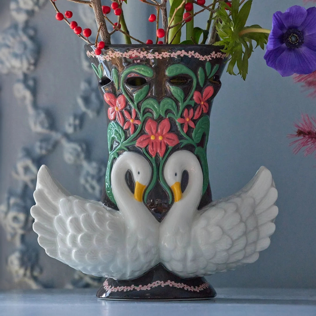 Vase en céramique noir avec des cygnes blancs et des motifs floraux rouges, rempli de branches rouges et de fleurs violettes.