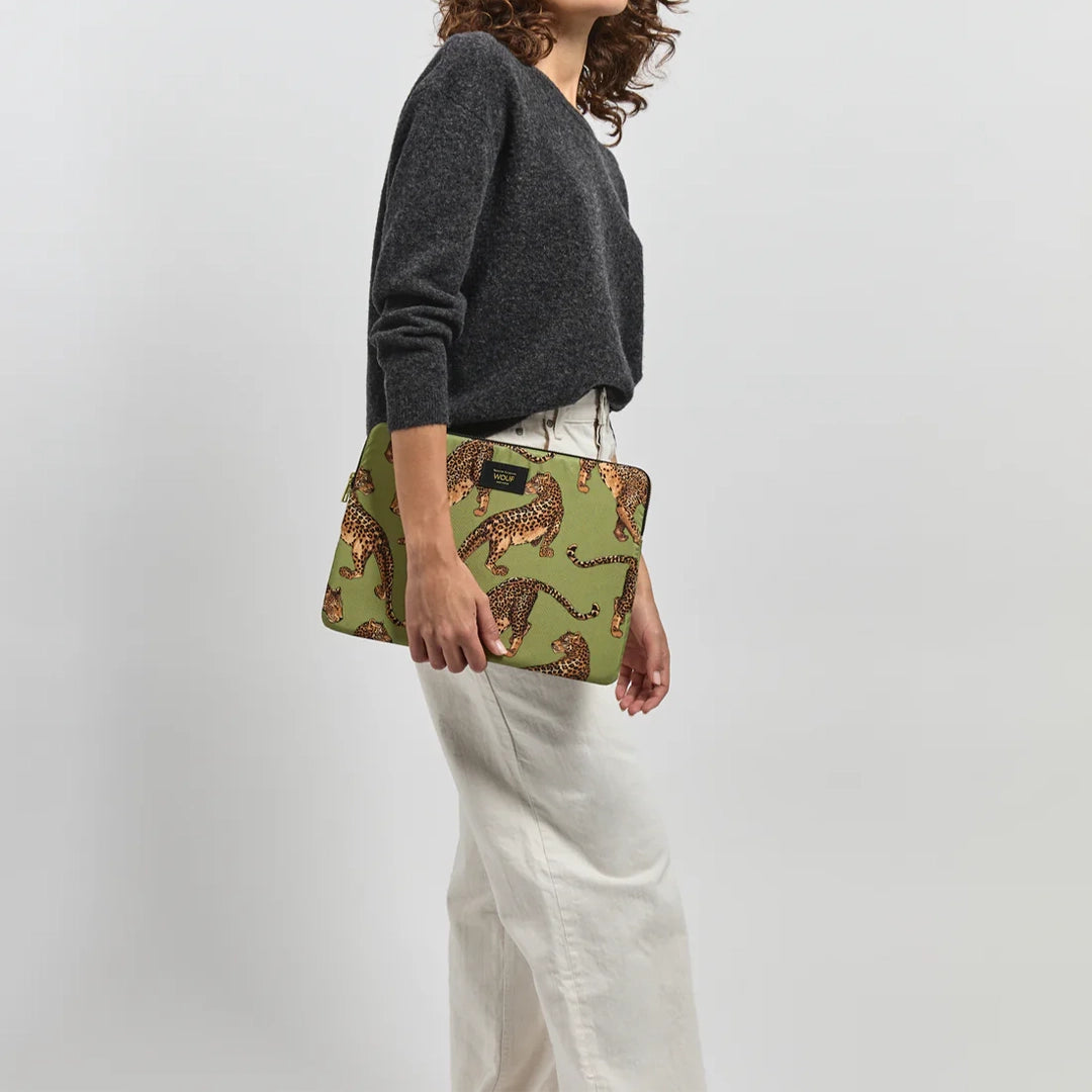 Personne marchant avec une housse d'ordinateur Olive Leopard de Wouf sous le bras, montrant des motifs de léopards sur un fond vert olive